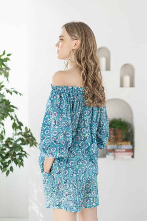 Woman in blue off-shoulder dress with floral pattern, standing indoors.