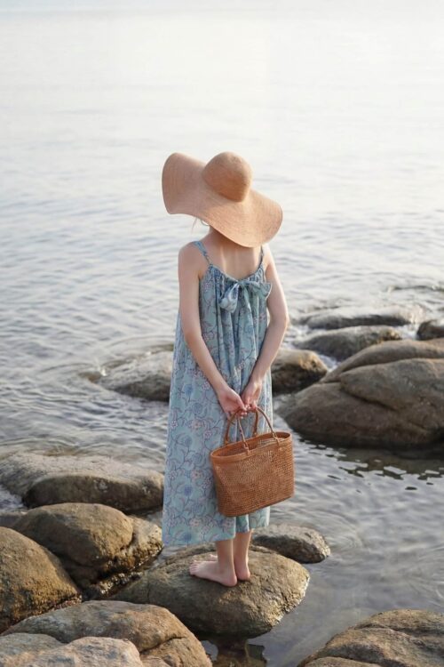 Girl standing on rocks by the sea with rainbow reflection in water.