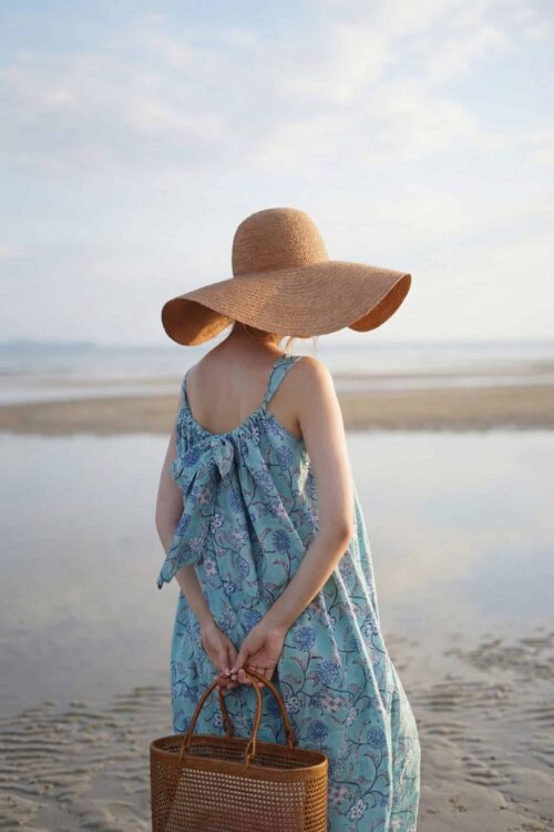 Rainbow over the beach with a woman in a blue dress and wide-brimmed hat.