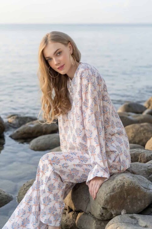 Woman sitting on rocks by the ocean wearing a floral patterned dress.