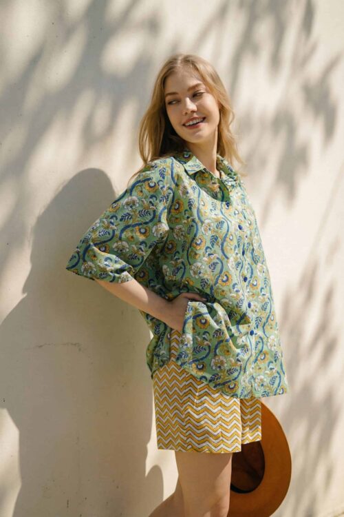 Bright, cheerful woman wearing a colorful patterned blouse and zigzag shorts.