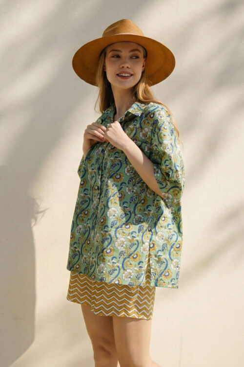 Elegant woman wearing a colorful patterned shirt and a wide-brim hat, enjoying a sunny day outdoors.