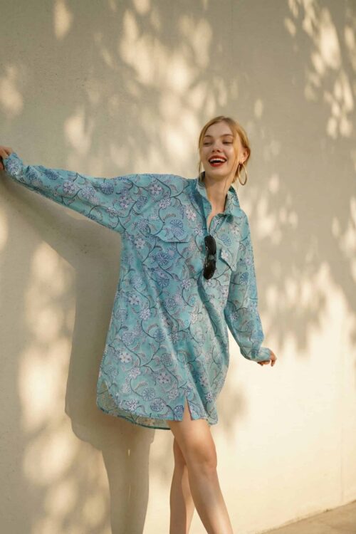 Fashion model wearing a blue patterned dress outdoors, smiling and enjoying sunlight.