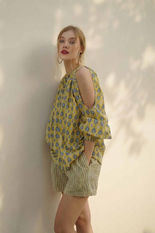 Elegant woman wearing a yellow floral blouse with cut-out shoulders and striped shorts, showcasing s.