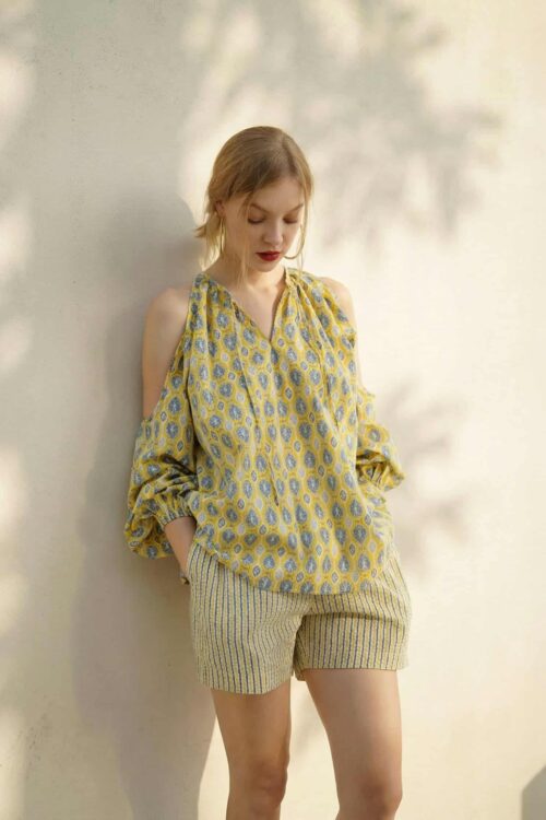 Woman in yellow patterned blouse and striped shorts for August style.