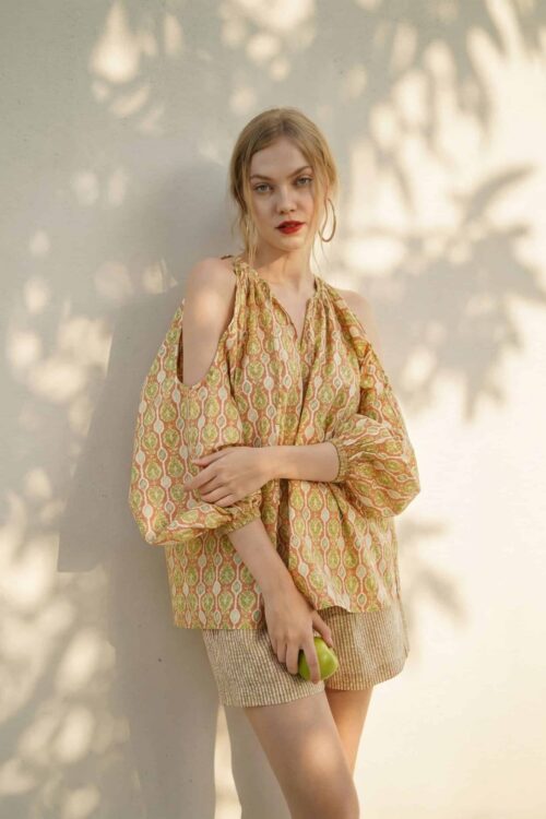 Woman in stylish summer outfit holding a green apple, sunny background.