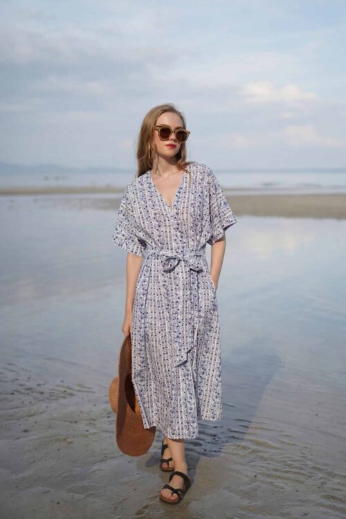 Woman in a floral beach dress walking on the shore in April.