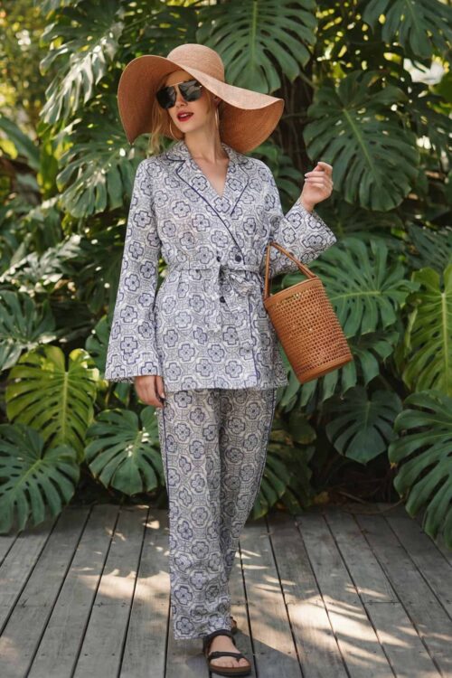 Elegant woman wearing a patterned suit, large sun hat, and sunglasses, holding a wicker basket in lu.