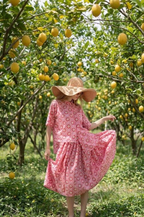 Woman in pink dress and wide-brim hat in lemon orchard during daytime.