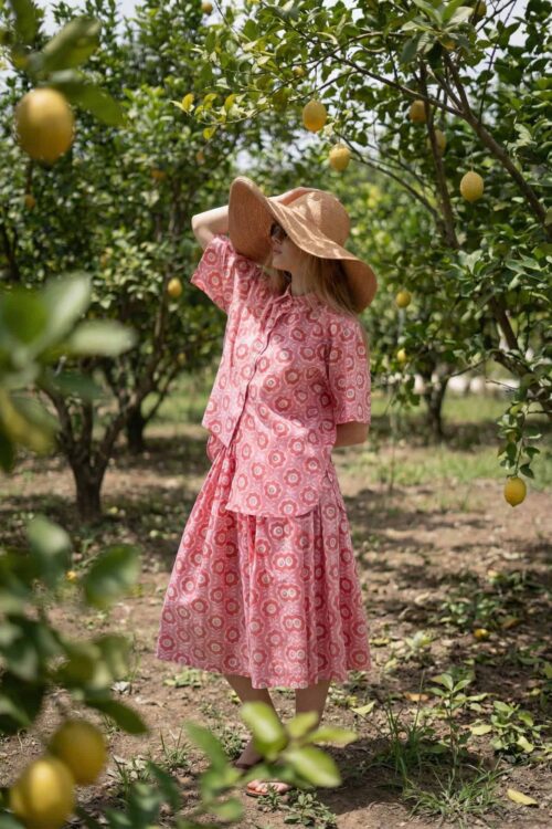 Woman in pink dress and wide-brim hat in lemon orchard.