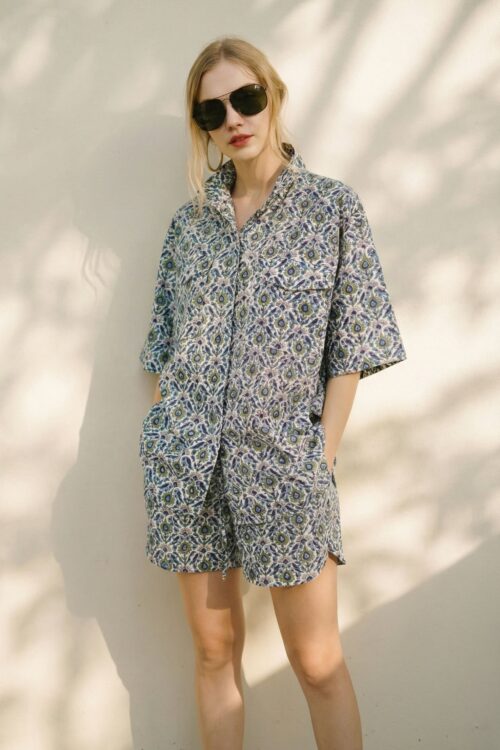 Stylish woman wearing a patterned summer shirt and shorts with sunglasses, embodying joy and relaxed.