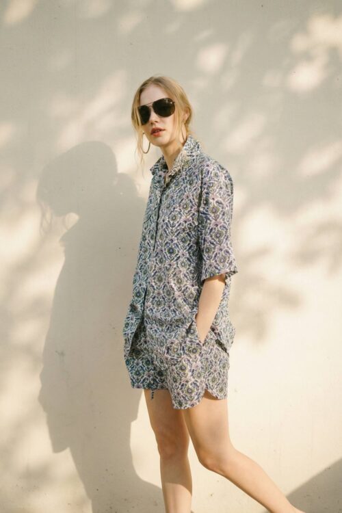 Stylish woman wearing sunglasses and a patterned shirt and shorts, embodying joy and relaxation.