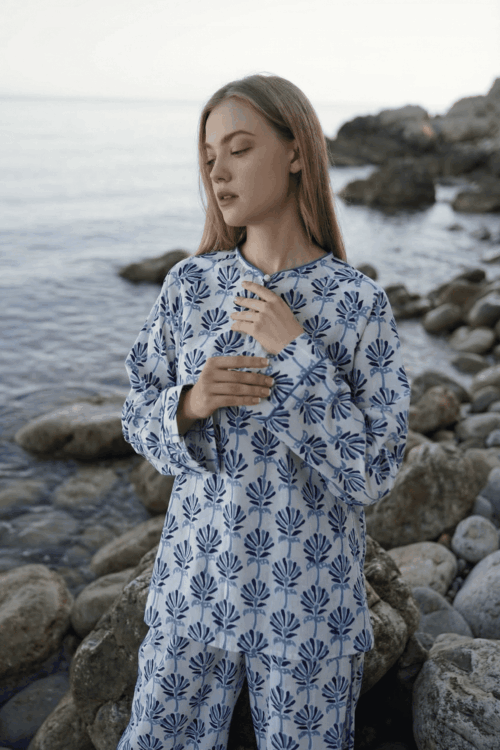 Elegant woman wearing a blue and white bubble-patterned pajama set by the rocky shoreline.