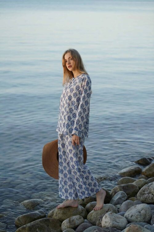 Elegant woman standing on rocks by the water in a floral dress.