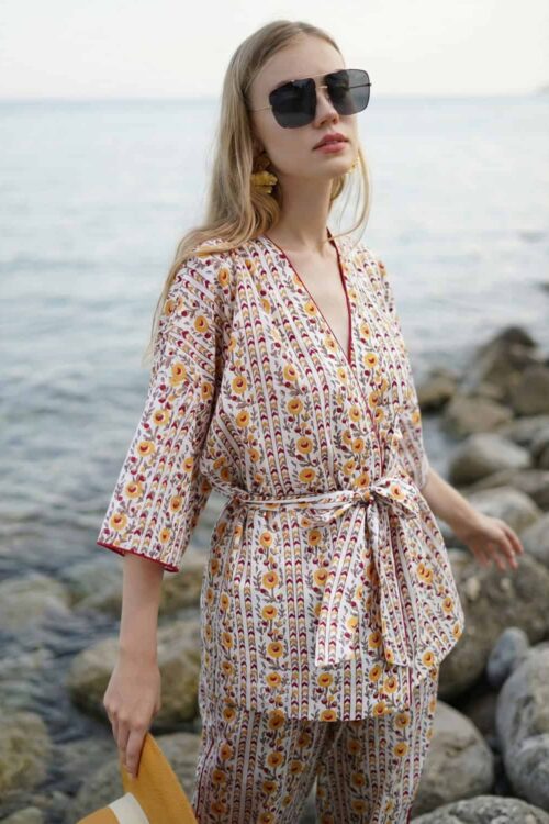 Stylish woman wearing a patterned beach cover-up with sunglasses by the sea.