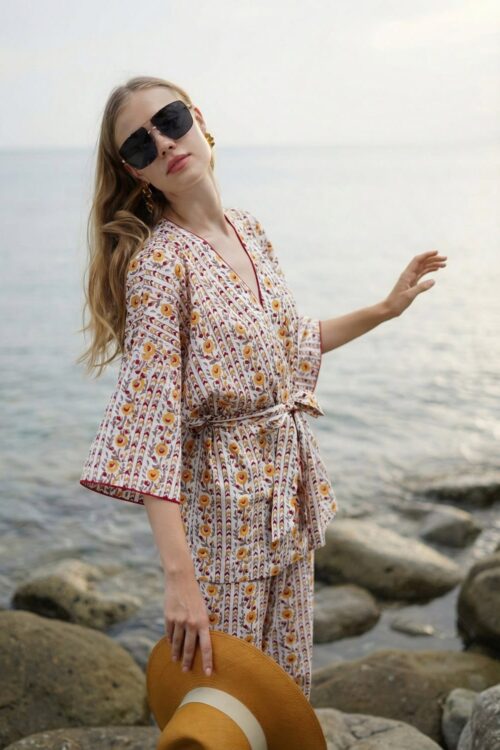 Woman in patterned dress and sunglasses standing on rocky shoreline during cloudy weather.