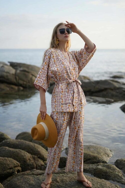 Stylish woman in patterned beachwear with hat and sunglasses by the sea on a cloudy day.