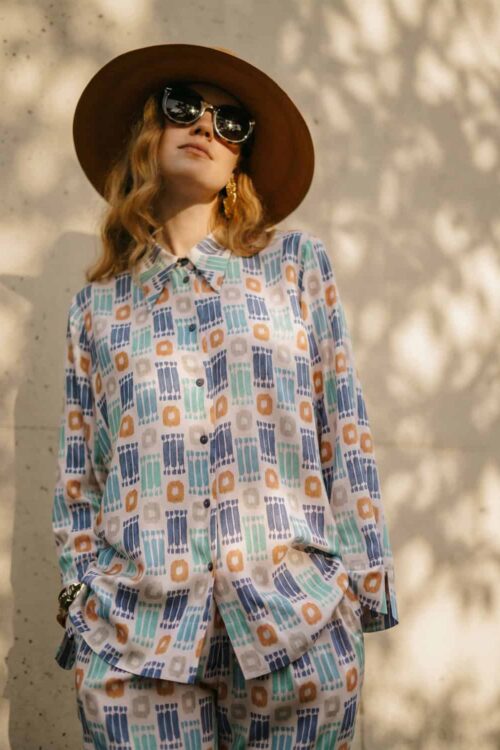 Elegant woman wearing a colorful, patterned outfit with a wide-brimmed hat and sunglasses.