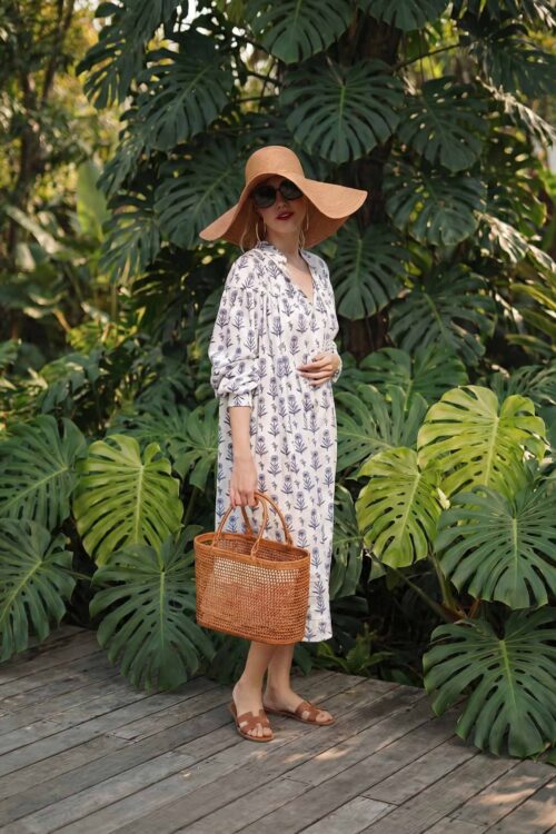 Summer fashion woman with large sun hat and wicker bag in lush tropical setting.