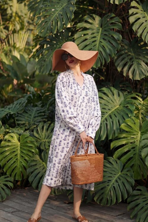 Elegant woman in a floral dress with a wide-brimmed hat and sunglasses, holding a woven basket, surr.