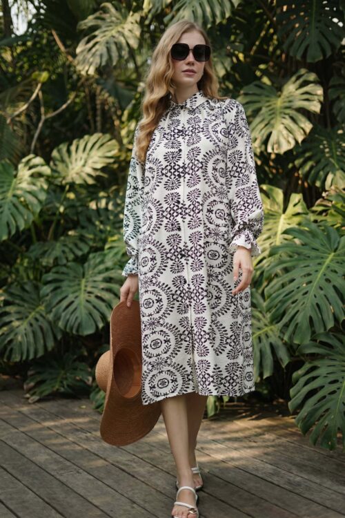 Woman in patterned dress standing among lush tropical garden foliage.