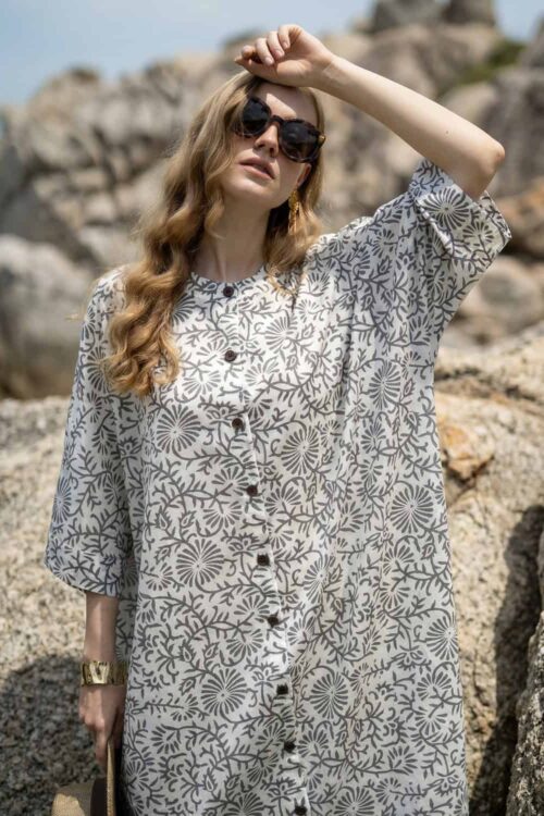 Woman in floral summer dress outdoors, sunny day, rocks background.