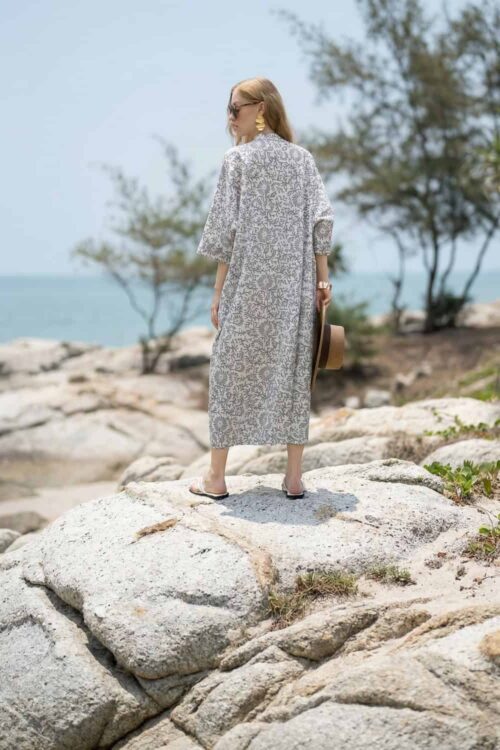 Woman in summer dress walking on rocks by the sea, enjoying sunny weather.