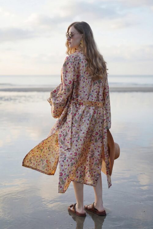 Woman in floral dress enjoying beach sunset, Waya Away new collection.