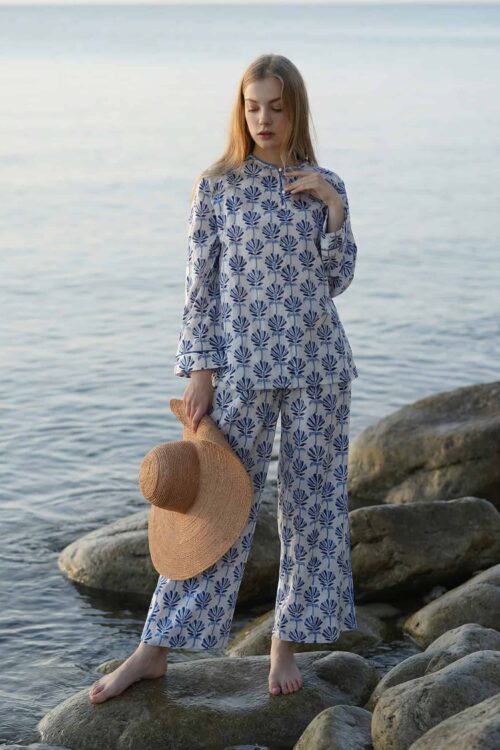 Woman in Waya Away beachwear standing on rocks by the sea, holding a straw hat.