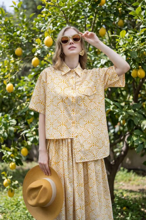 Woman in yellow patterned outfit with hat in lemon orchard.