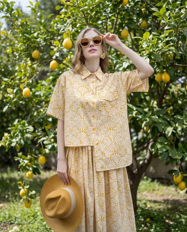 Woman in lemon-patterned fabric outfit standing in lemon orchard.