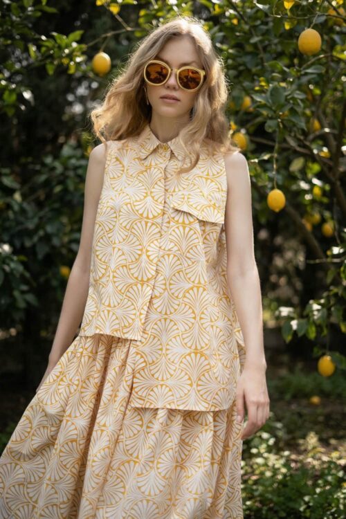 Stylish woman wearing a yellow geometric patterned dress and sunglasses outdoors among lemon trees.