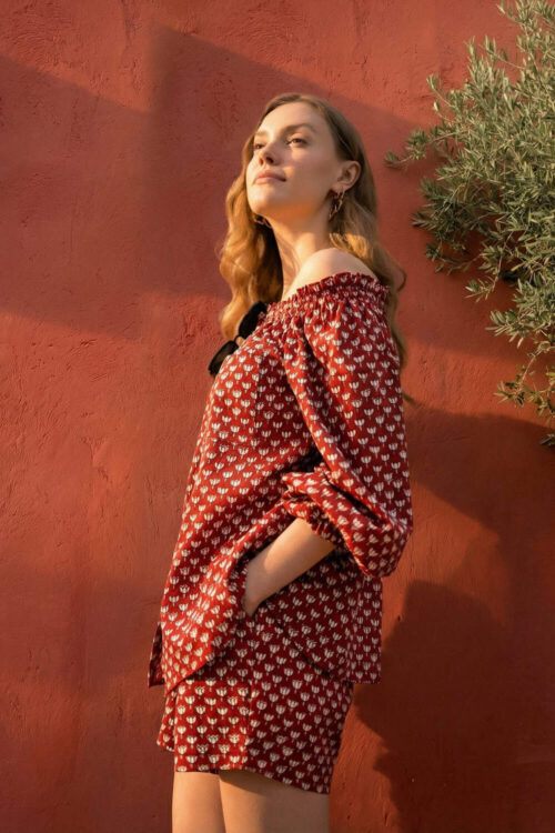 Woman in red patterned dress standing outdoors against a red wall.